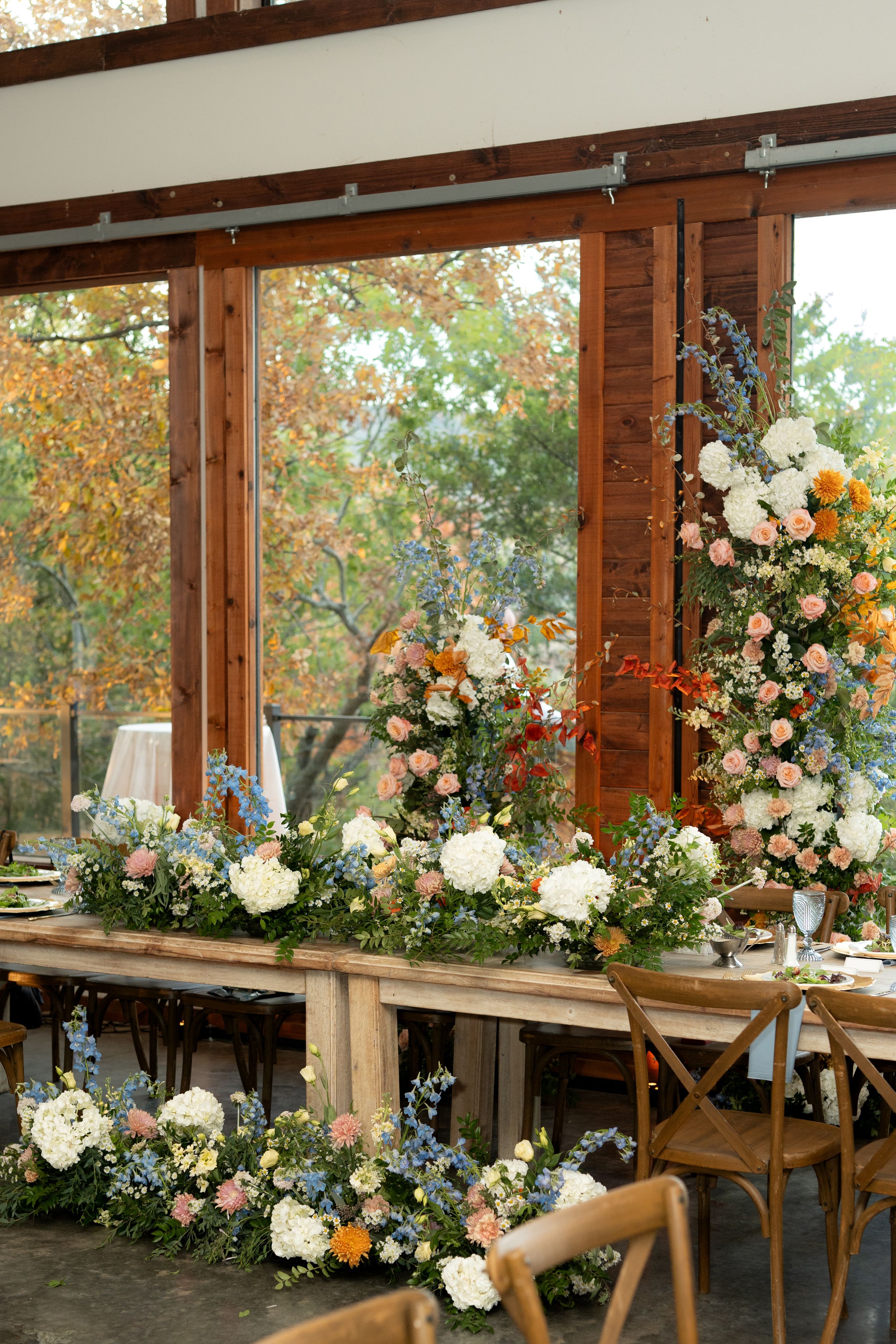 Rustic wooden reception tables decorated with elegant white and peach floral arrangements.