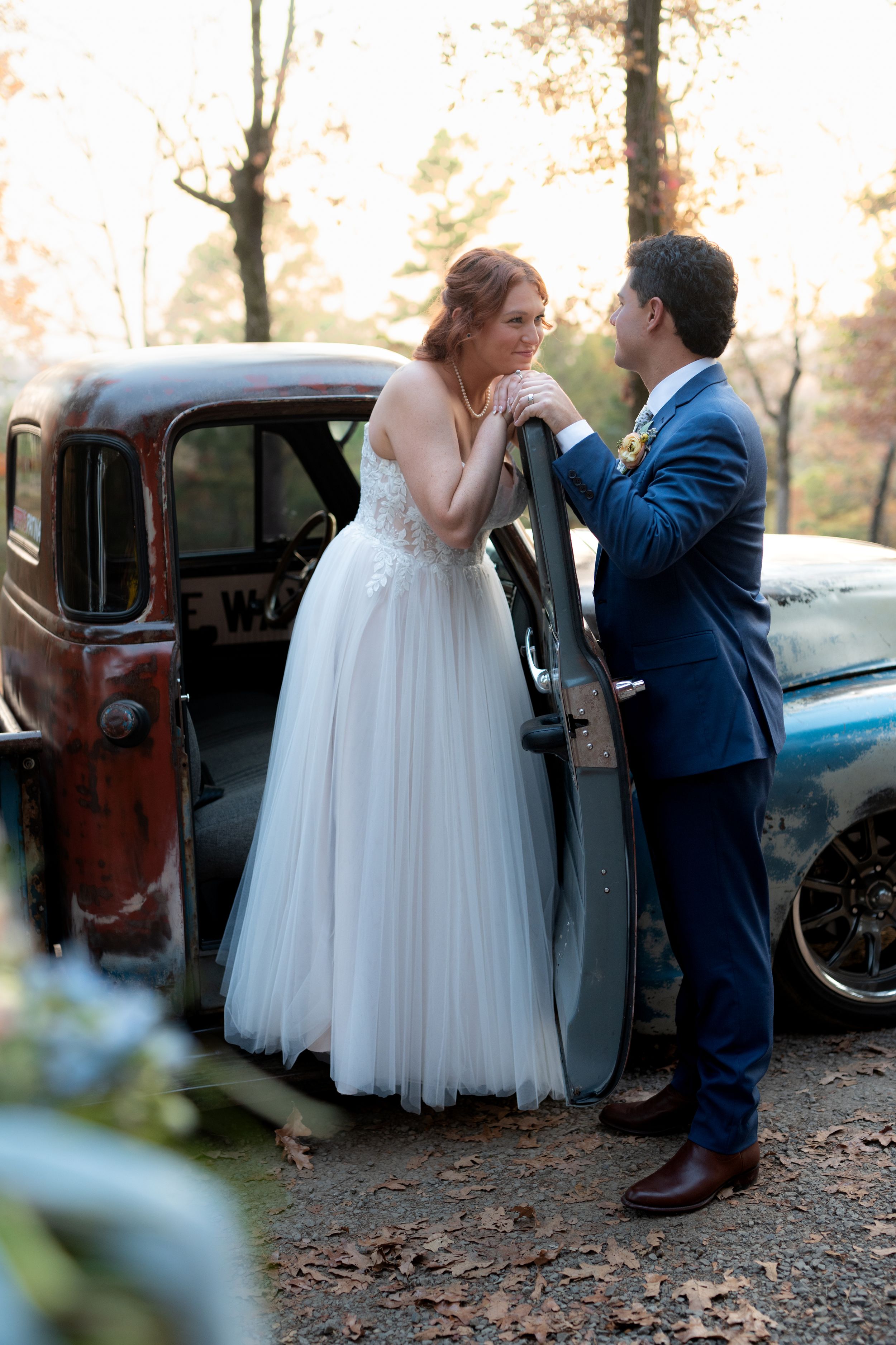 Wedding couple sharing a moment by vintage car surrounded by autumn trees.
