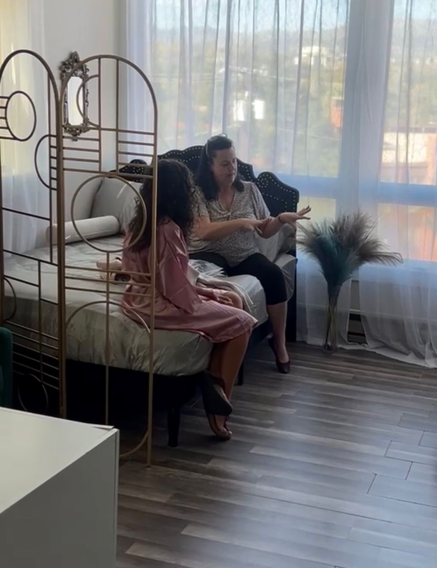 People relaxing on vintage metal bed frame near sunny window.