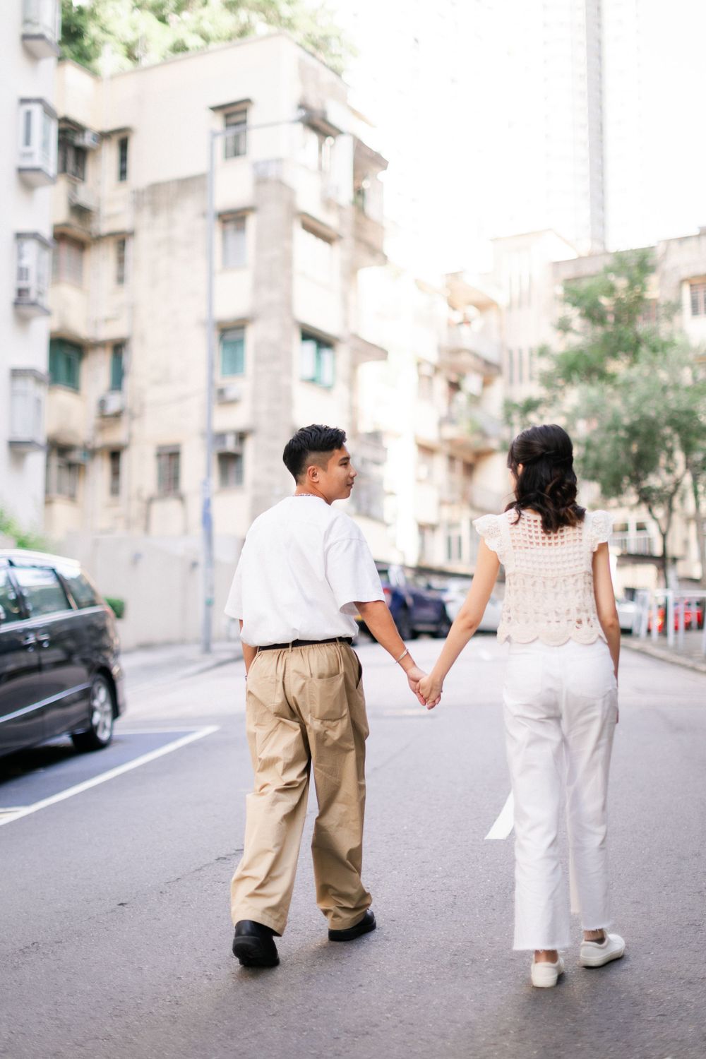 A couple holds hands while walking down a sunny urban street lined with buildings.