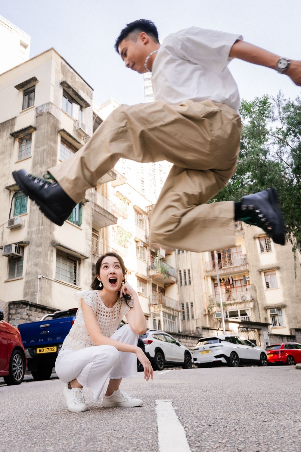 A man jumps in the air while a woman crouches below him on a city street.