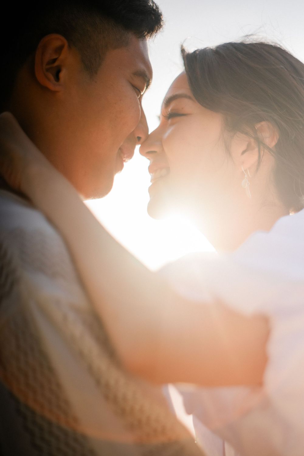 Couple sharing an intimate moment with foreheads touching, backlit by warm golden sunlight.