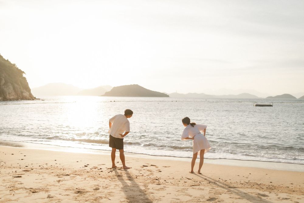 Couple walking on a sandy beach at sunset with mountains and calm ocean in the background.