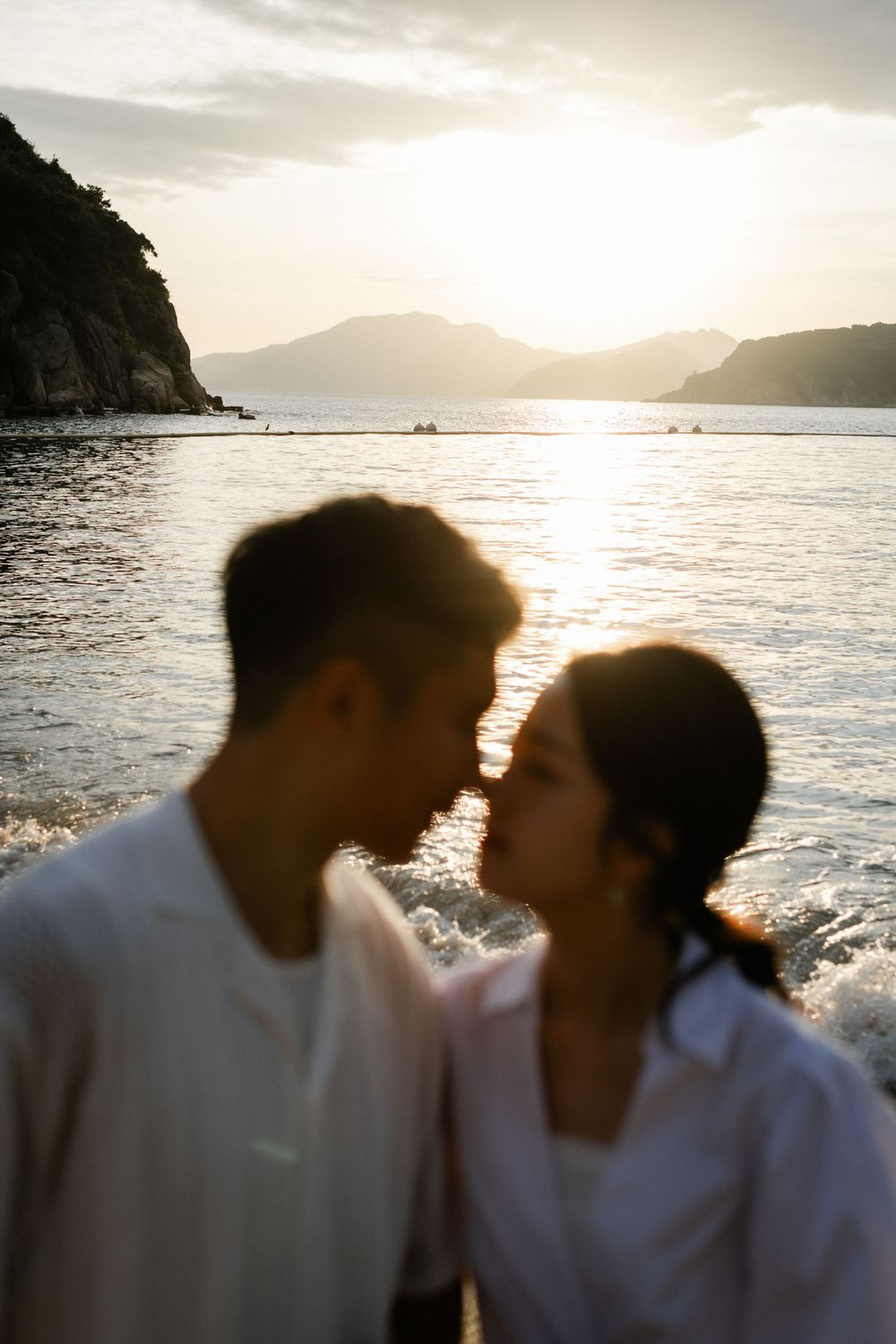 Silhouetted couple sharing intimate moment nearly kissing against stunning golden ocean sunset backdrop.