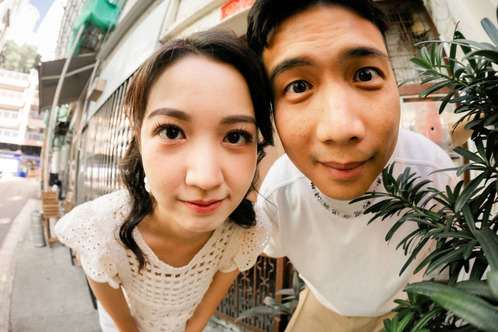 Fun close-up fisheye shot of a smiling Asian couple on a city street.