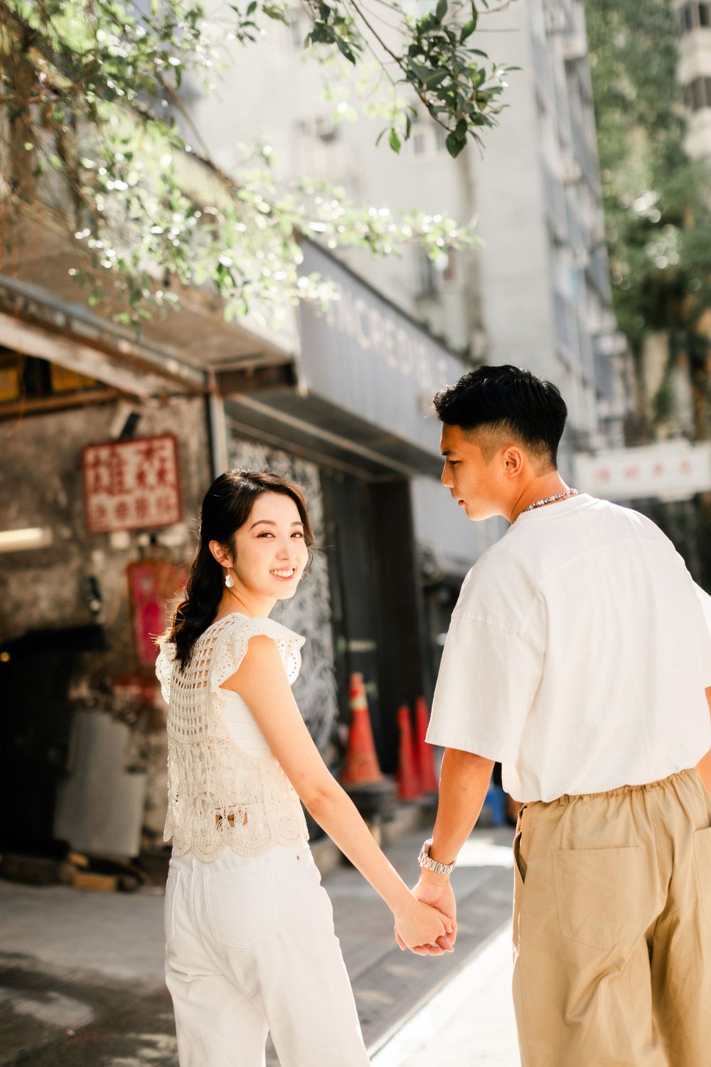 Smiling Asian woman looks back while holding hands with her partner on a city street.