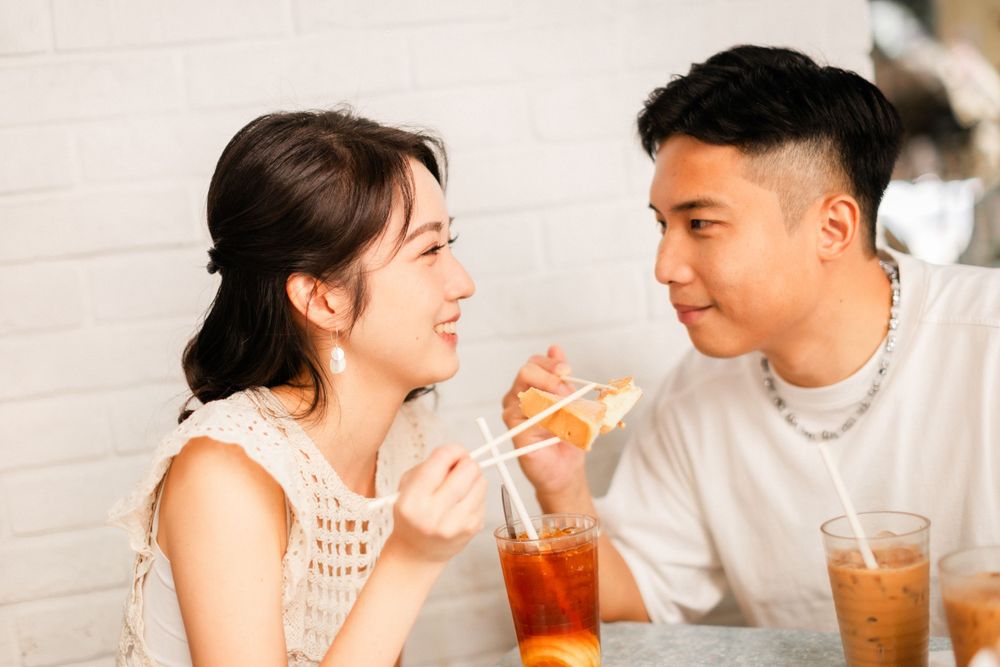 Young Asian couple sharing food and drinks at a cafe, smiling at each other intimately.