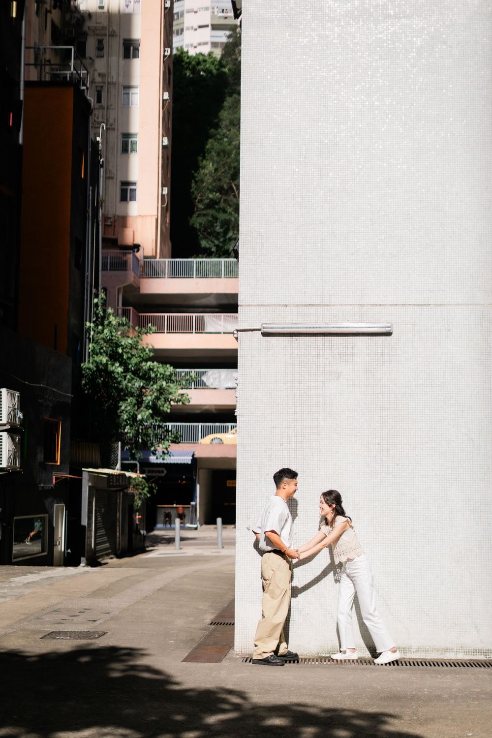 Asian couple holding hands and leaning against white tiled wall in urban city street.