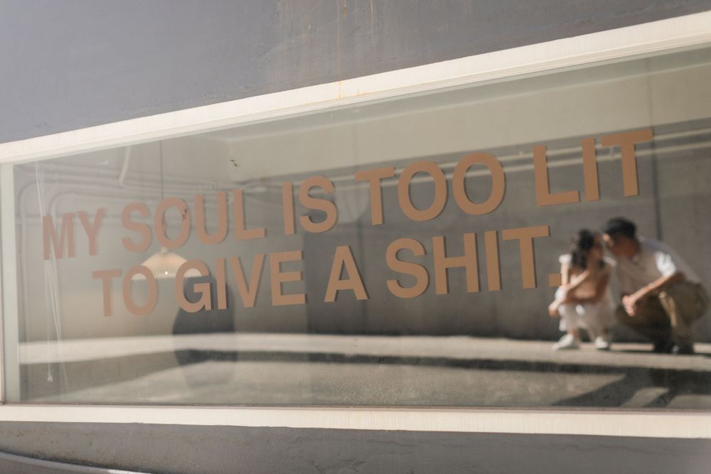 Glass panel with bold text reading MY SOUL IS TOO LIT TO GIVE A SHIT in urban setting.