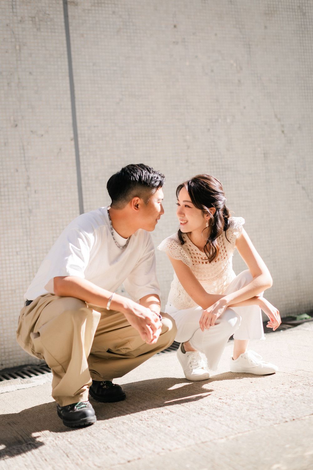 Young Asian couple crouching and gazing at each other lovingly against a white wall.