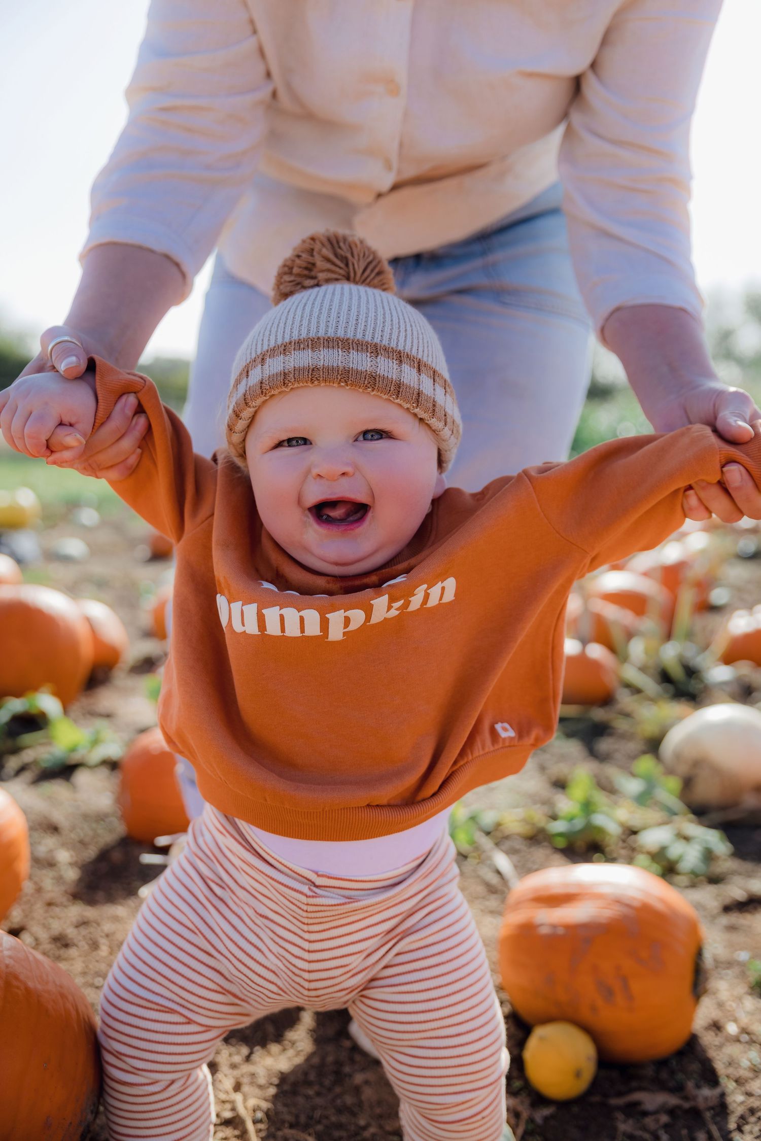 Infant in striped pants and orange pumpkin sweater smiling in pumpkin patch. Photographer. Hull. East Yorkshire.