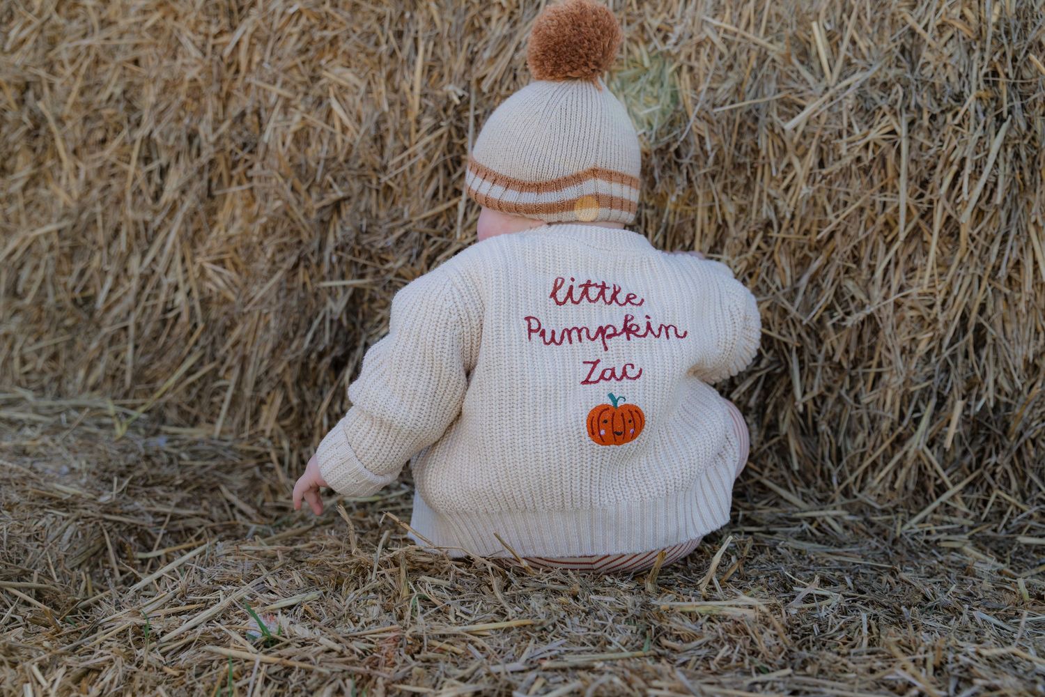 Row of white knit baby hats with pumpkin designs displayed on hay bales. Photographer. Hull. East Yorkshire.