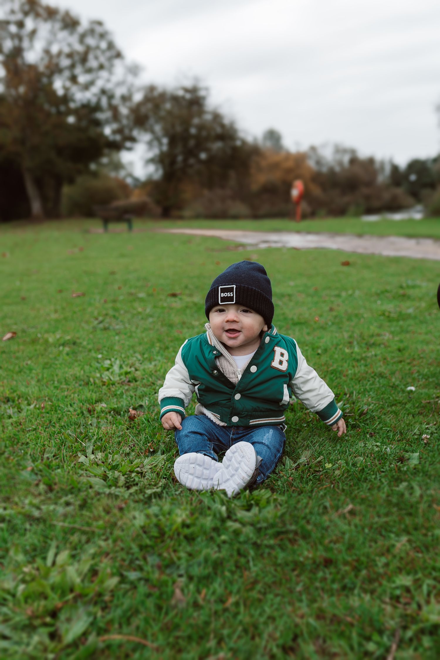 A small child in a varsity jacket plays on green grass during a cloudy day. Photographer. Hull. East Yorkshire. Photography