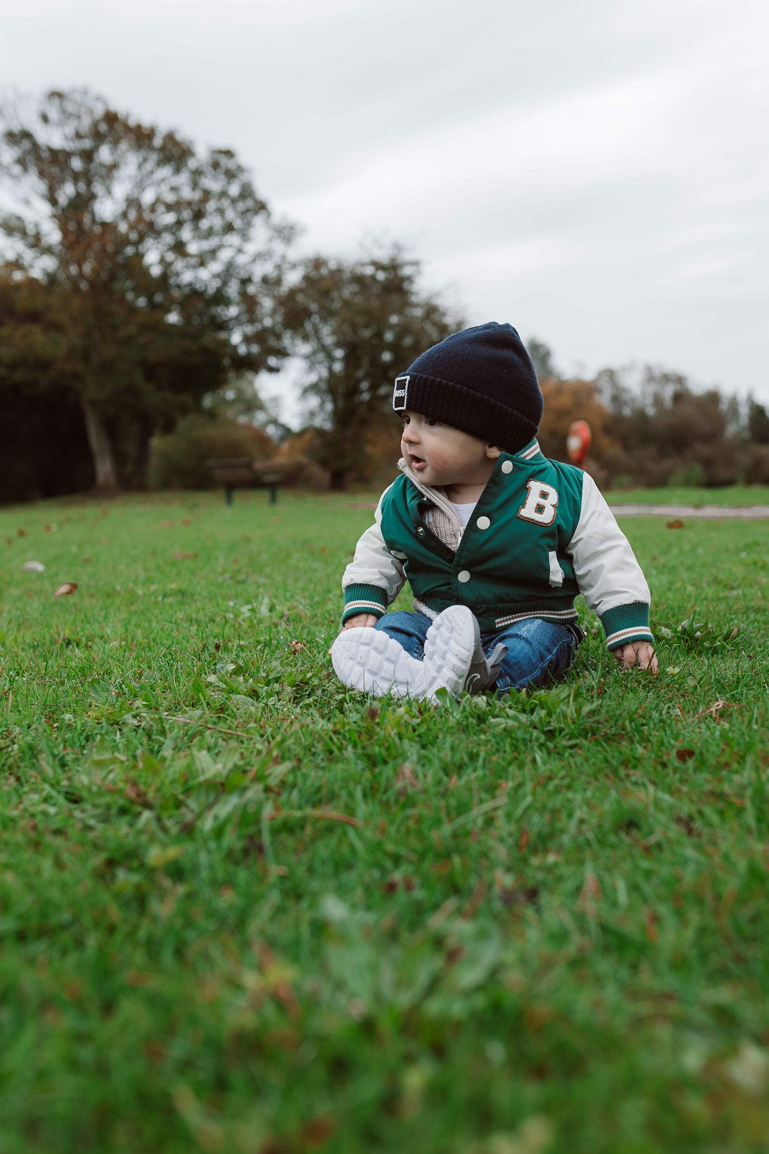 Close-up shot of a child lying in green grass wearing a varsity jacket and beanie. Photographer. Hull. East Yorkshire. Photography