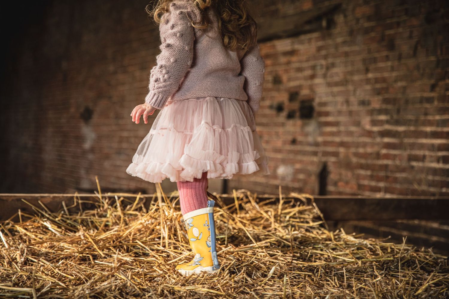 Pink tulle dress and yellow boots create a whimsical scene against rustic brick walls and hay. Photographer. Hull. East Yorkshire. Photograp