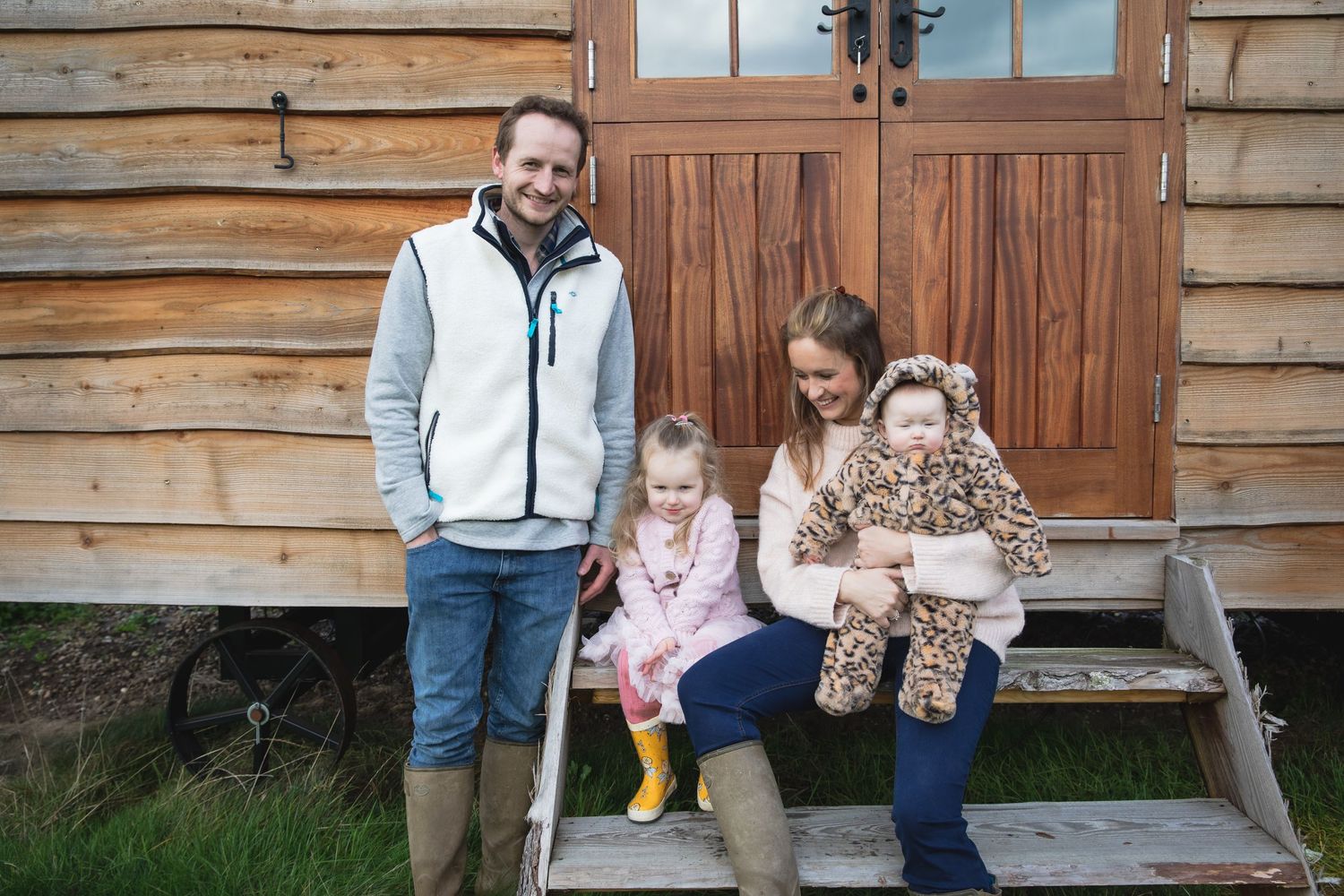 Family members sit together on a rustic wooden bench outside a log cabin on a sunny day. Photographer. Hull. East Yorkshire. Photography