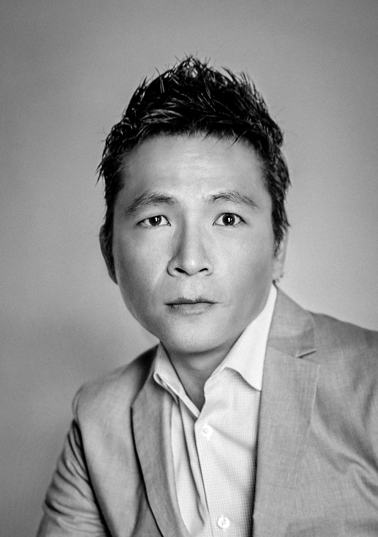 Professional black and white headshot of person in suit jacket against plain backdrop.