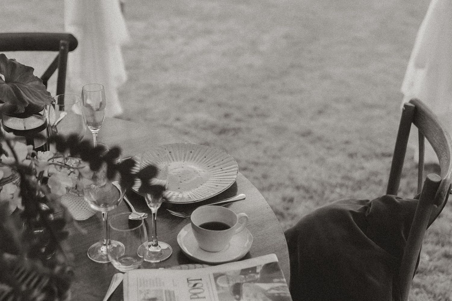 Black and white image of an elegant outdoor table setting with wine glasses and a straw hat.