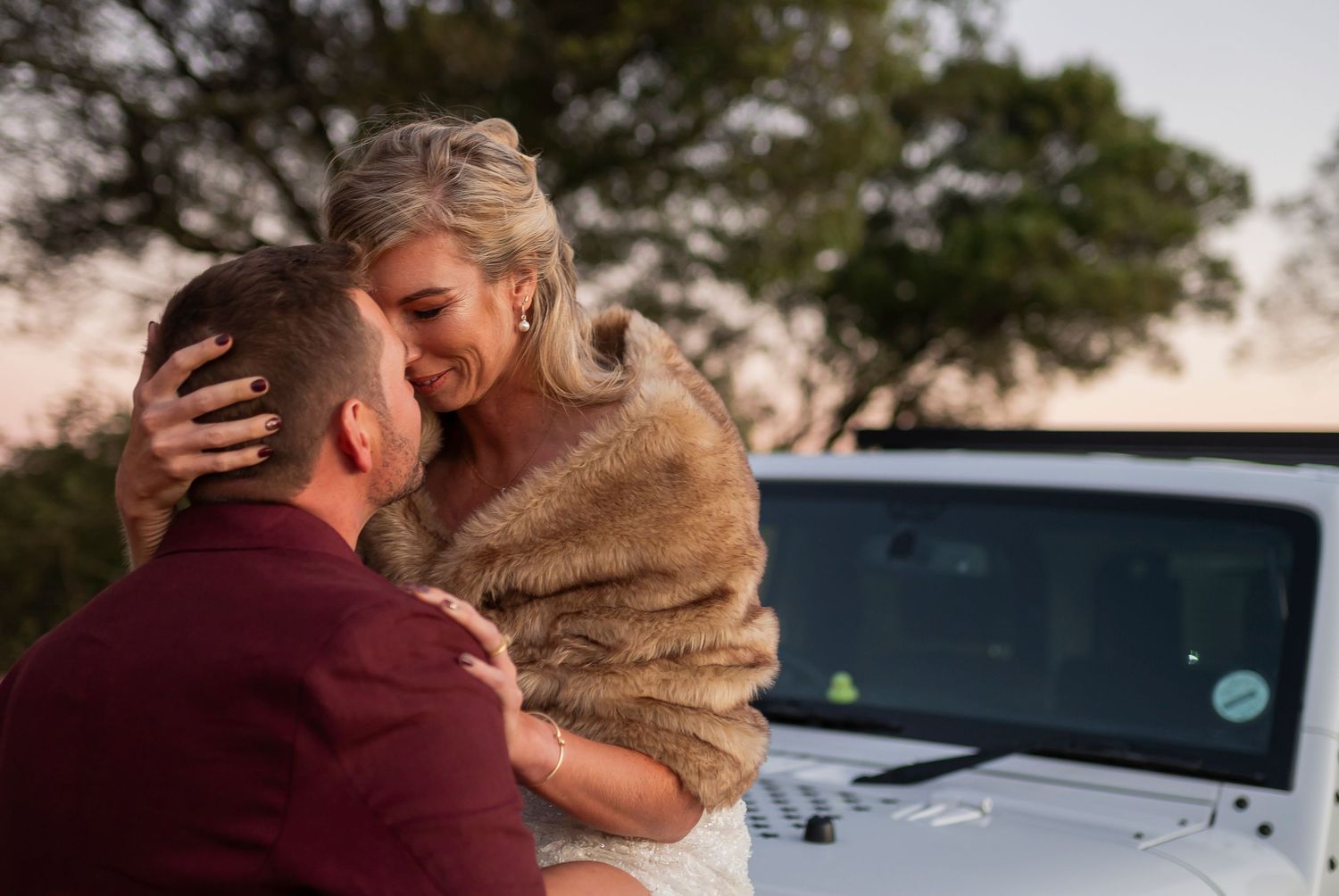 Two people share an intimate embrace while sitting in the back of a pickup truck at sunset.