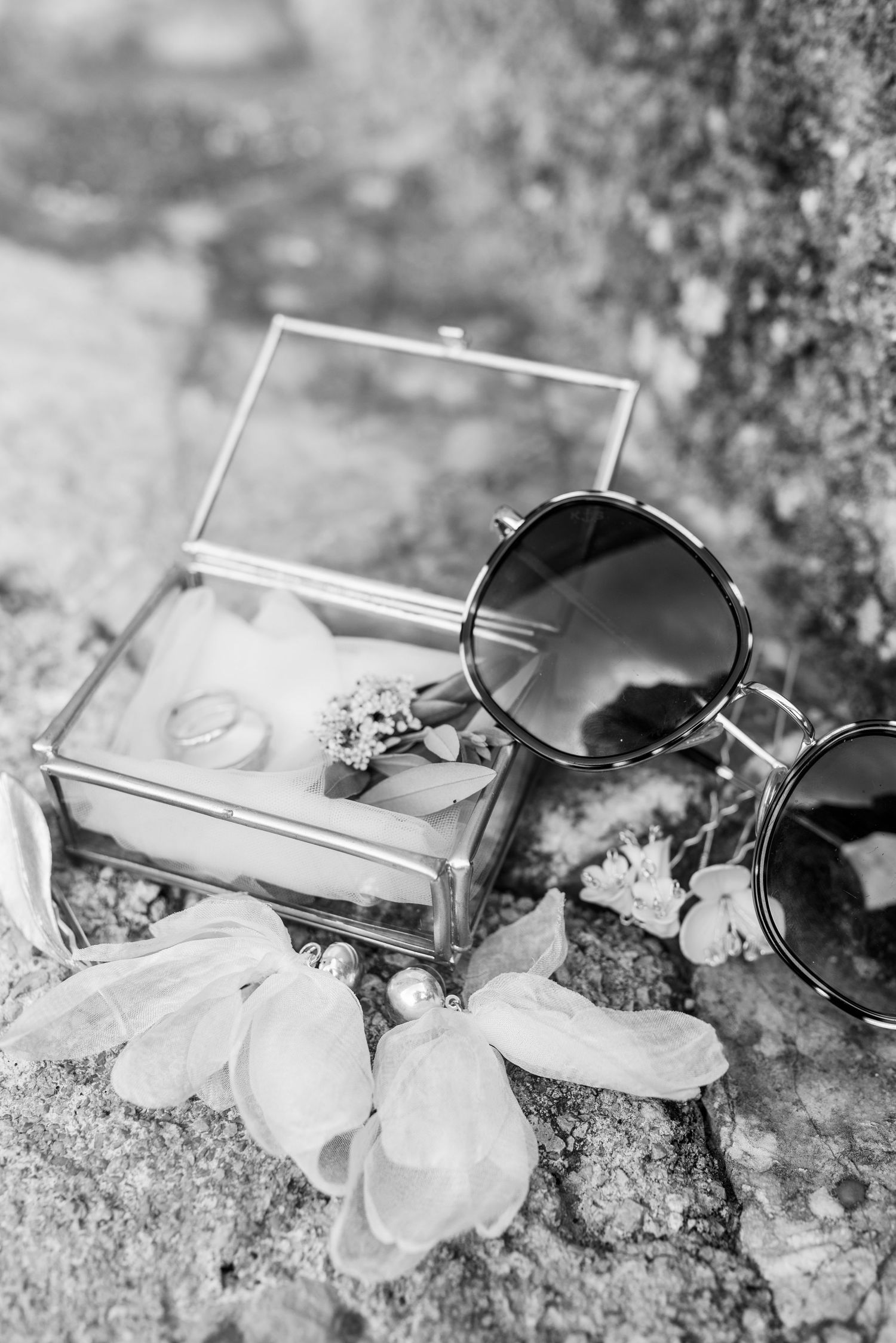 Ein Detailsbild in Schwarz-Weiß von der Ringbox und den Eheringen auf einer mallorquinischen Steintreppe mit der Sonnenbrille der Braut.