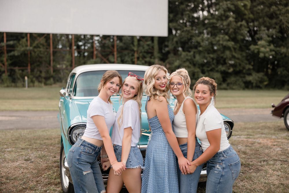 A group poses outdoors in coordinated denim and white outfits with their hands covering their faces playfully.