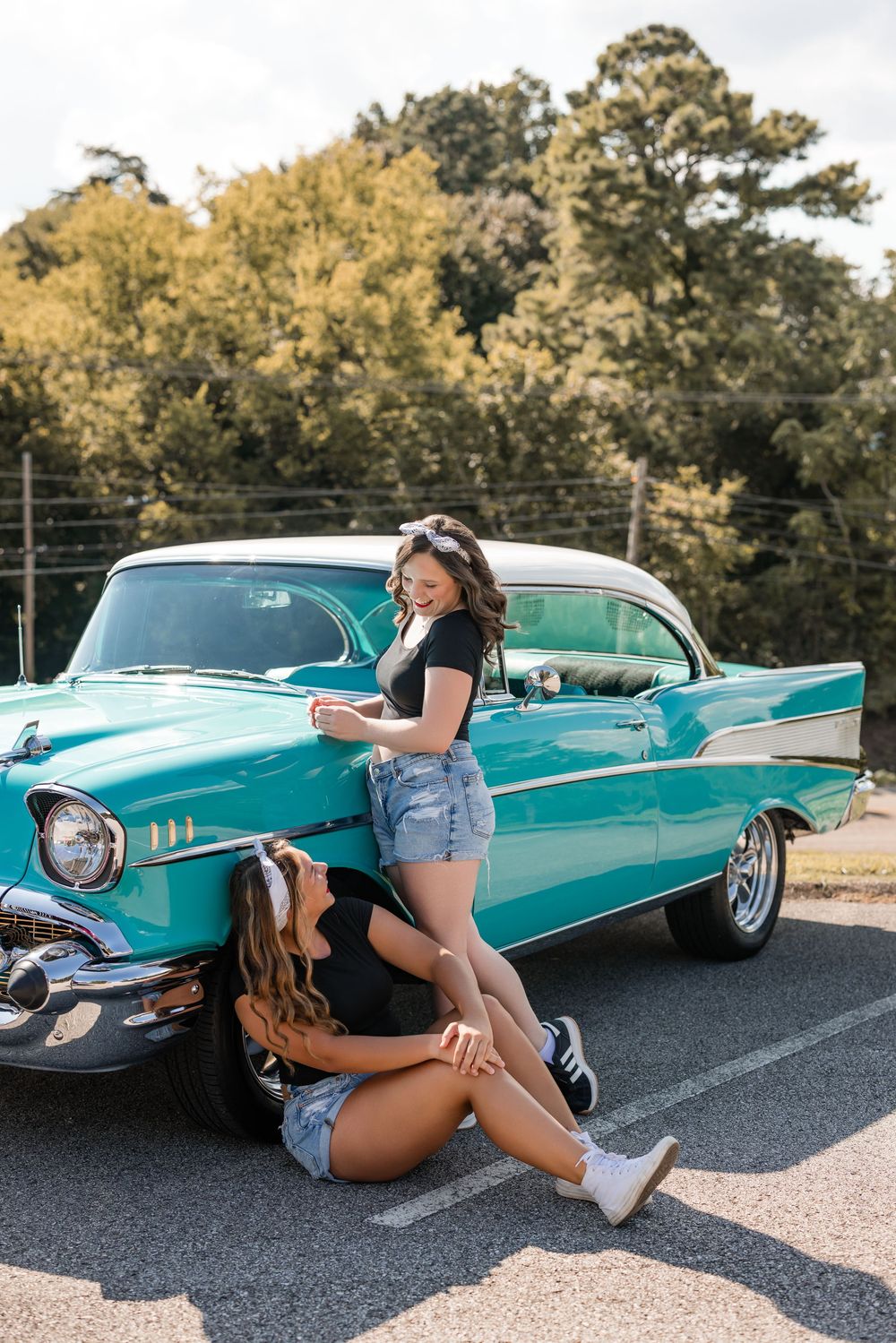 Two people pose playfully in front of a vintage turquoise Chevrolet Bel Air on a sunny day.