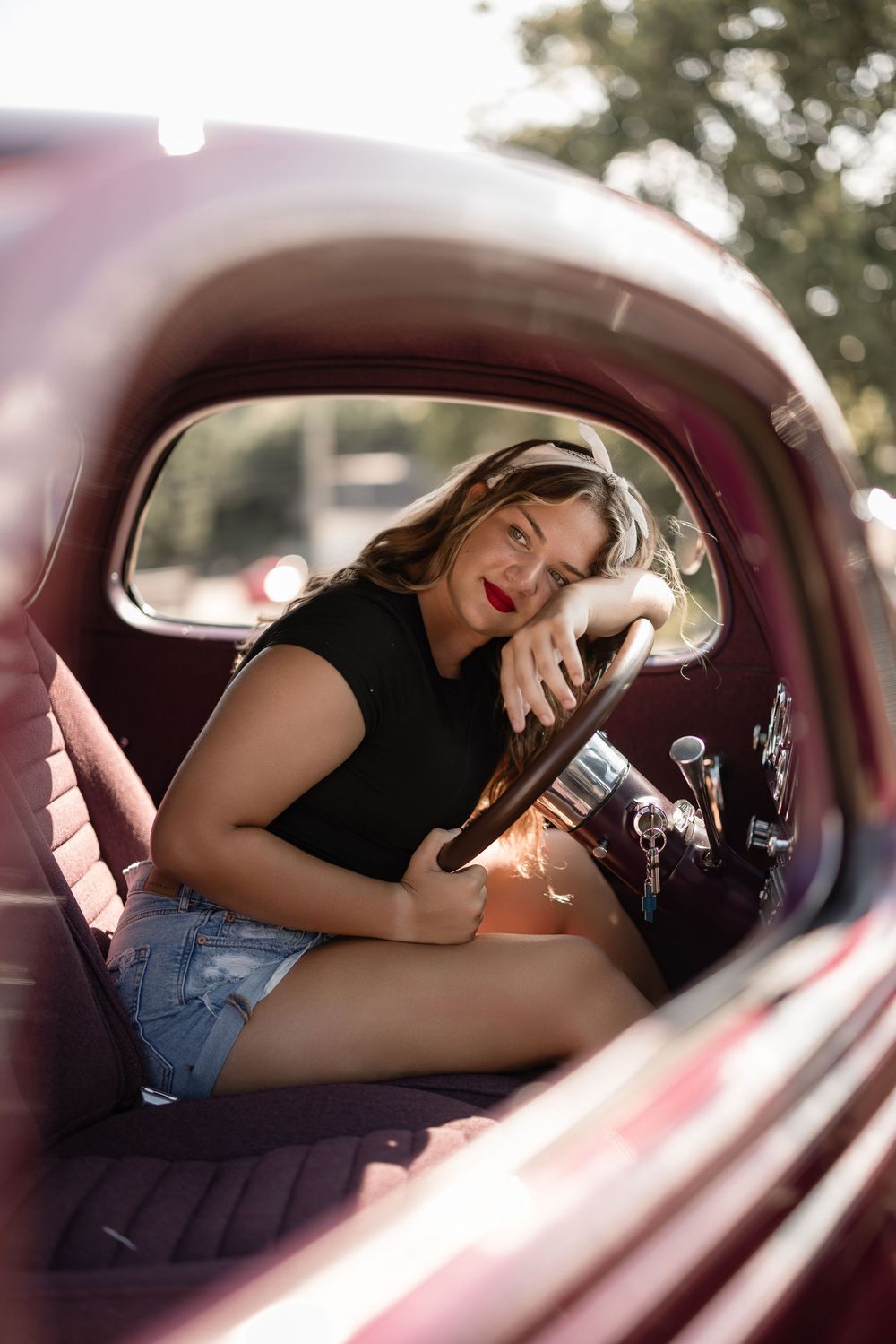 Through the window of a classic burgundy car, someone relaxes in vintage-inspired casual attire.