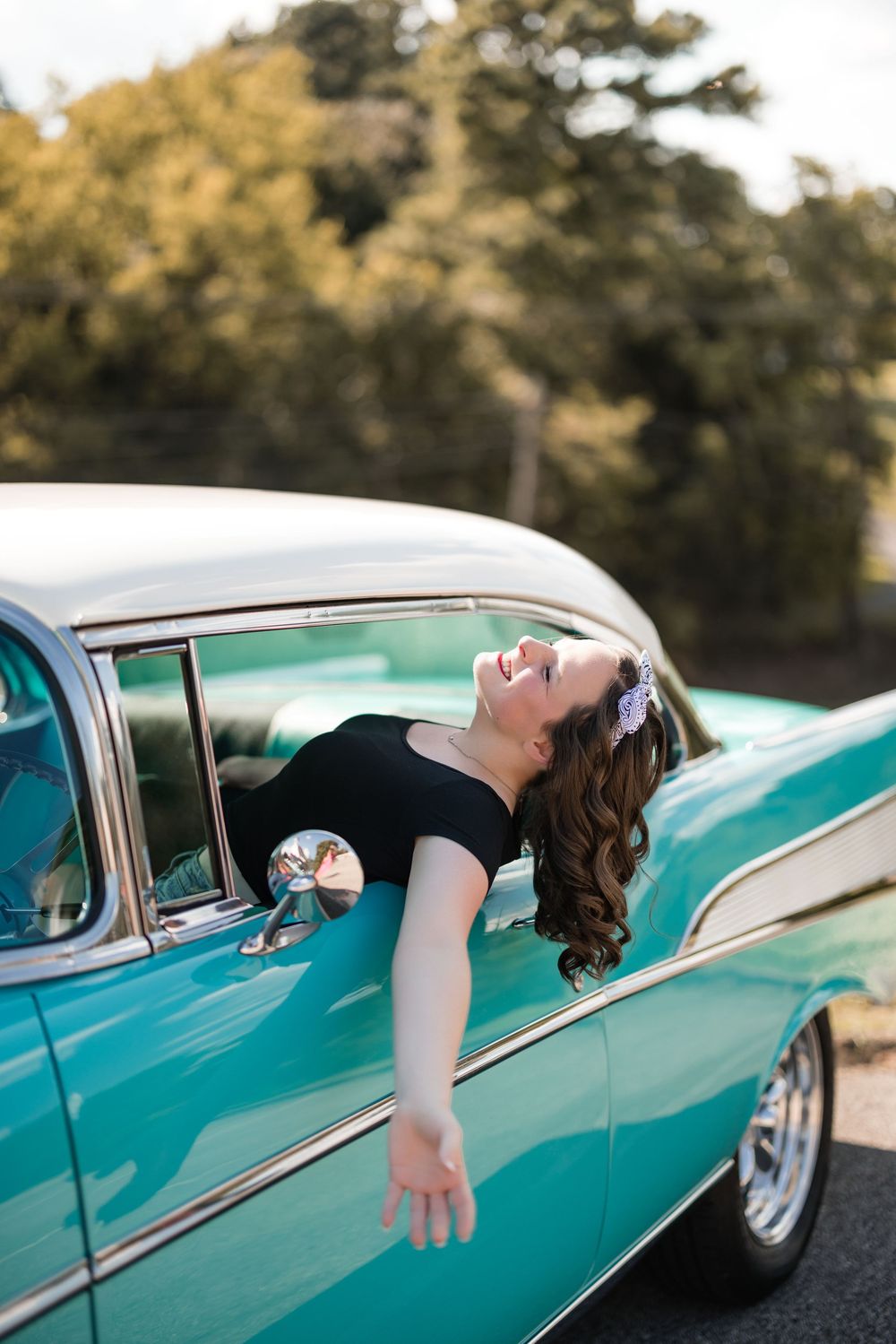 Person leans out of classic turquoise car window with dramatic pose against blurred background.