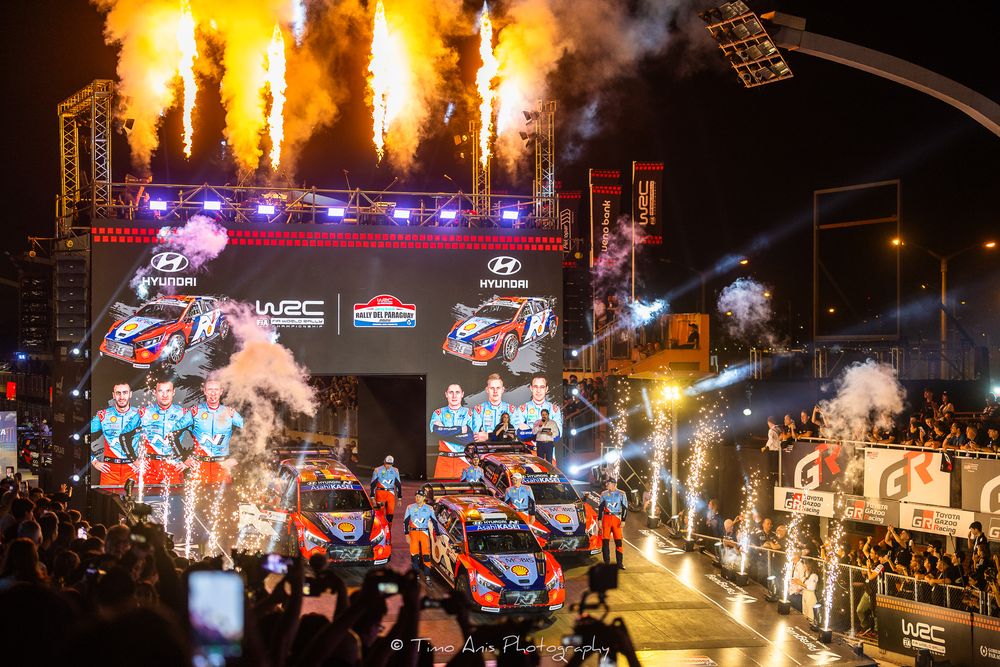 Dramatic race car launch with orange flames and pyrotechnics during an exciting nighttime motorsports event.