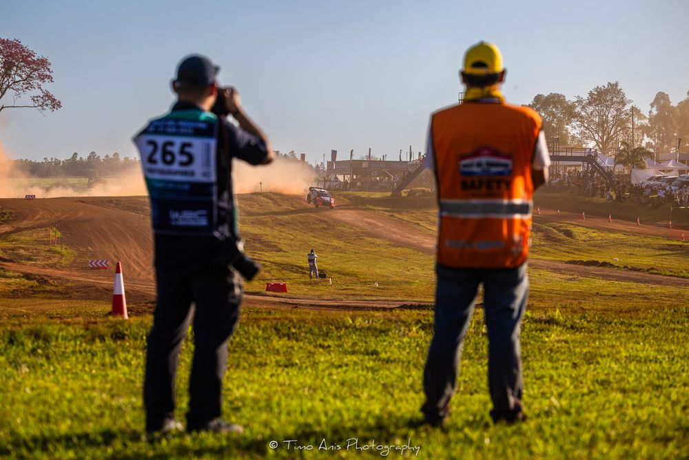 Two surveyors with safety gear working in a green field during sunset.