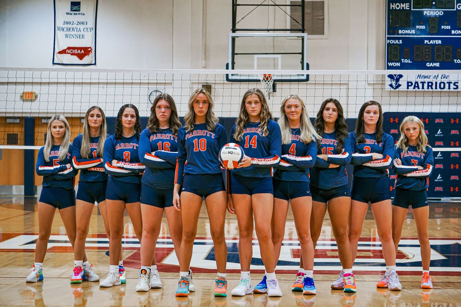 Nine Patriots volleyball players in blue and red uniforms pose together in a gymnasium.