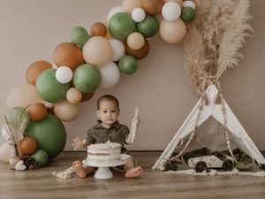 Boho-themed first birthday party setup with balloon garland, teepee tent, and smash cake in neutral earth tones.