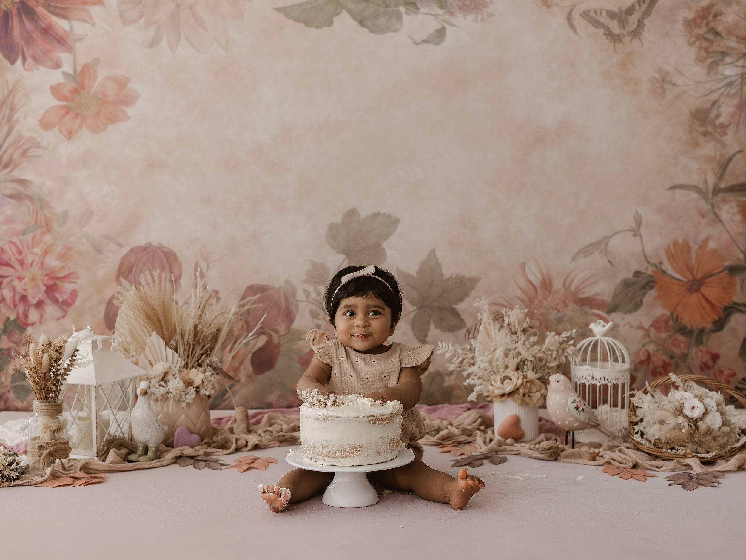 A collection of vintage birdcages and floral decorations arranged against a soft pink floral backdrop.