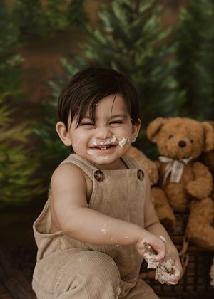 Happy toddler in corduroy overalls laughs with cake on face during festive Christmas cake smash session.