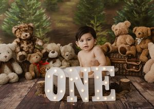 Baby's first birthday photo with illuminated ONE sign surrounded by teddy bears and Christmas trees.