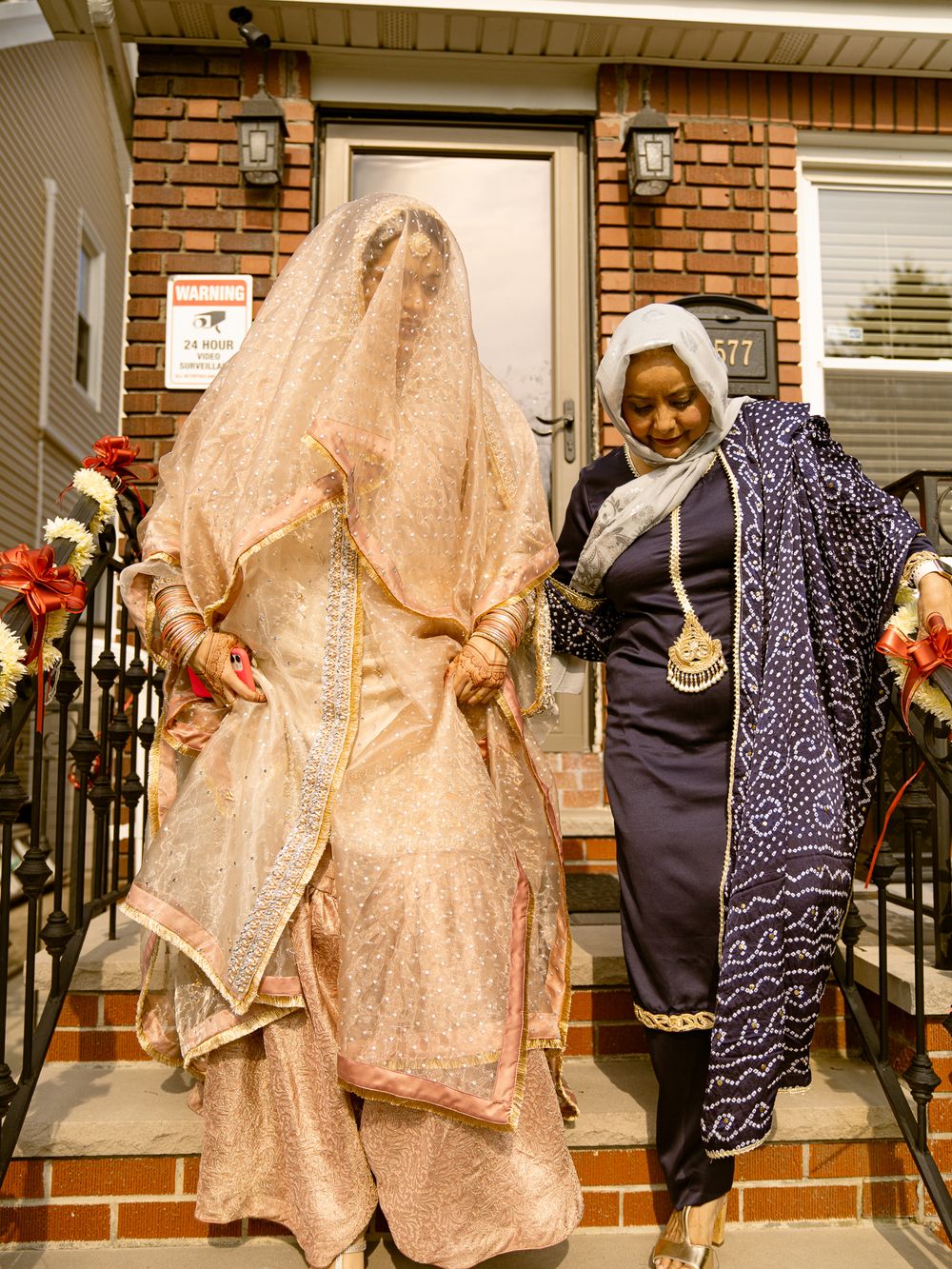 Traditional wedding guests in colorful attire and sparkly dresses gather outside a brick building entrance.