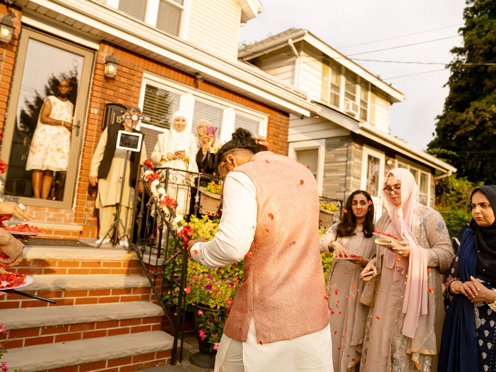 Wedding celebration with guests taking photos outside a traditional brick house with decorative flowers.