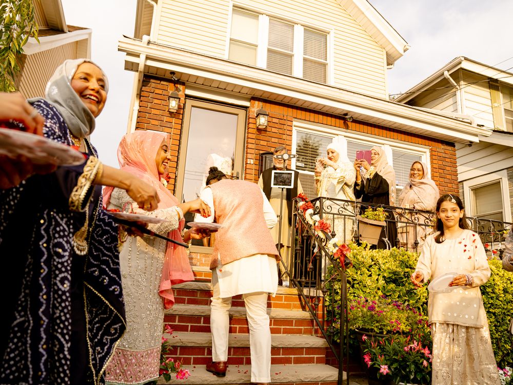 Wedding party members gather on front steps of house during outdoor celebration.