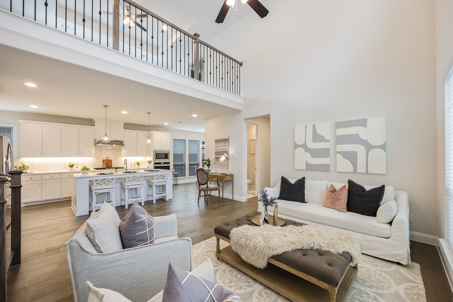 Contemporary open-concept living room with white walls, ceiling fan, and modern grey and white furniture arrangement.