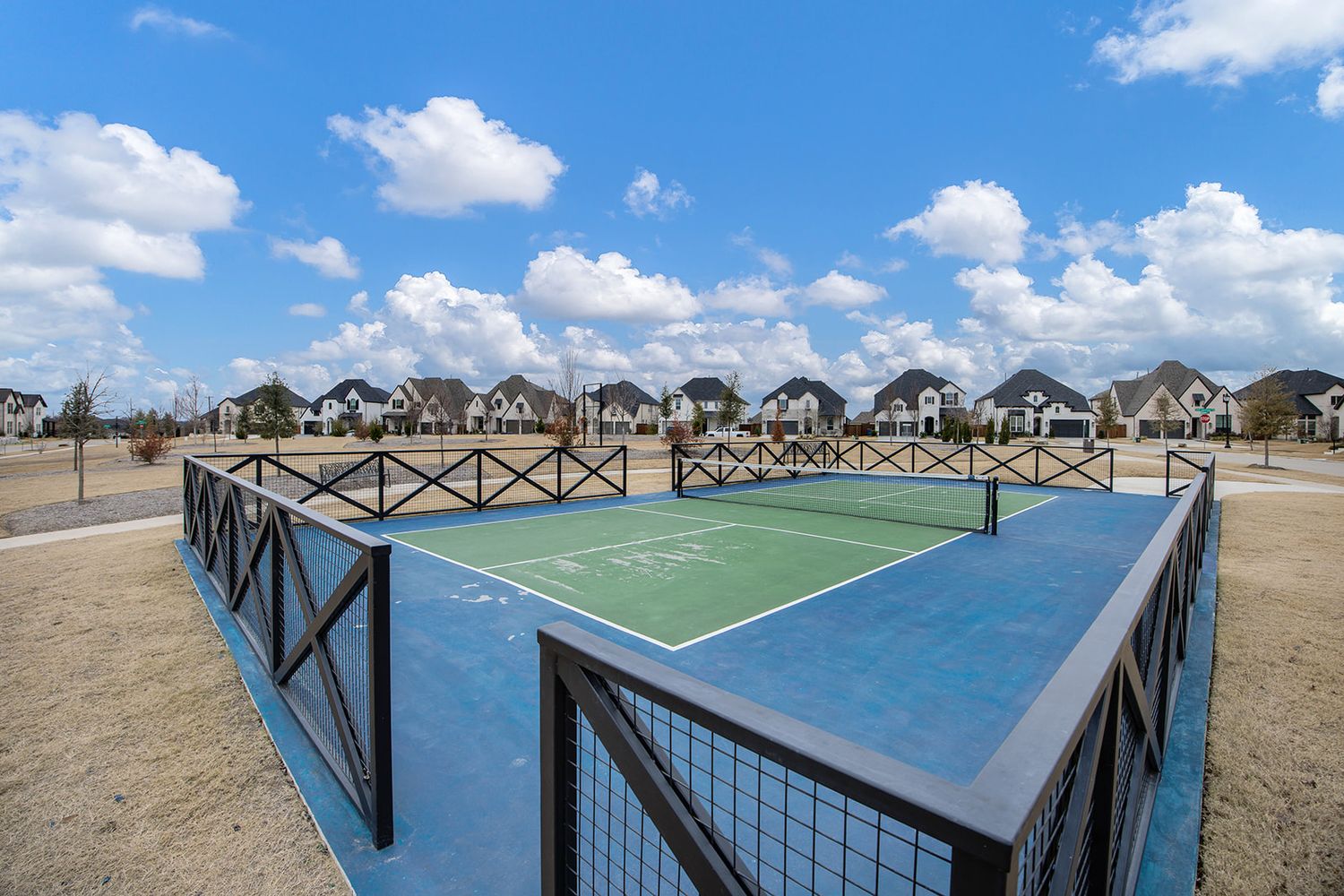 Outdoor pickleball courts overlooking the ocean with wooden fencing and beach houses visible in the background.