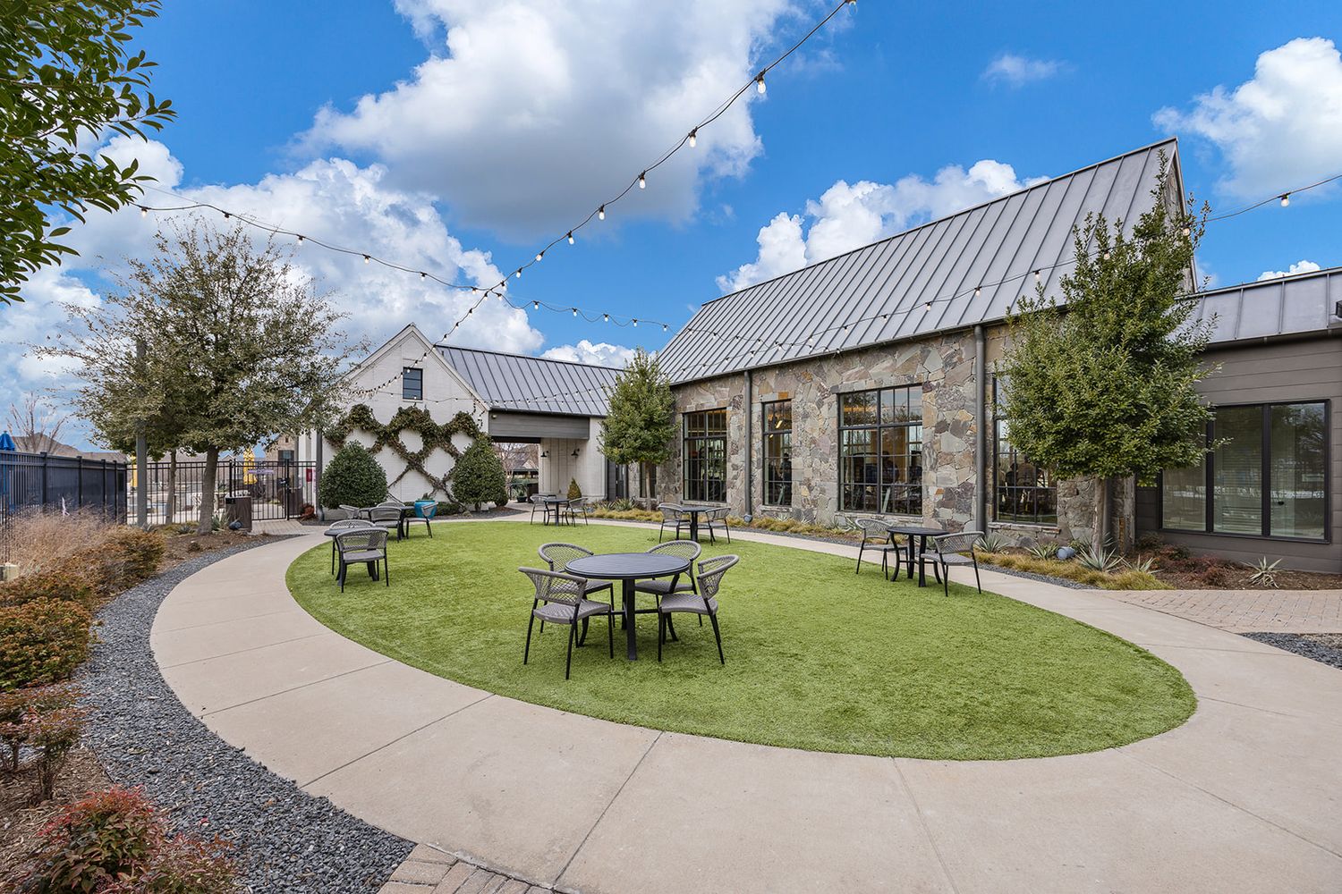 Modern residential development featuring curved walkways, metal roofs, and landscaped grounds under partly cloudy skies.