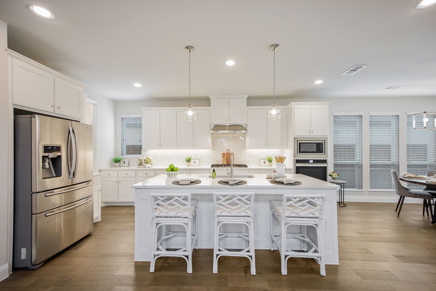 Modern white kitchen with stainless steel appliances, large center island, hardwood floors and pendant lighting.
