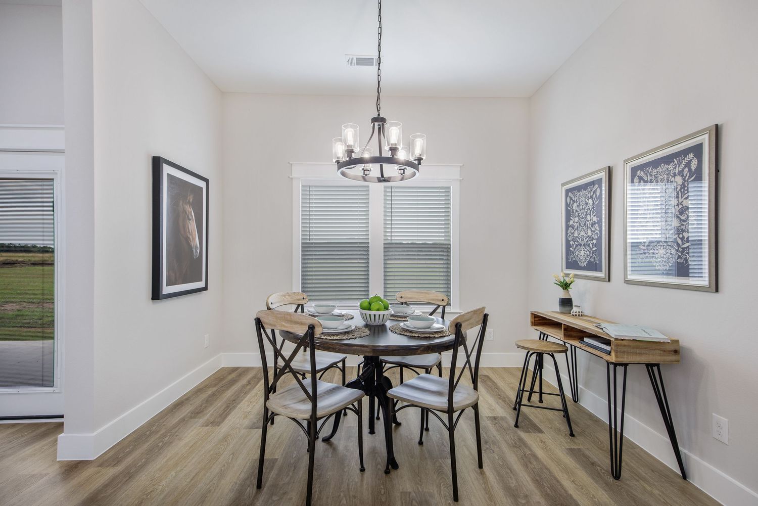 Modern dining nook features round table with metal chairs, wood console table and black chandelier in bright white room.