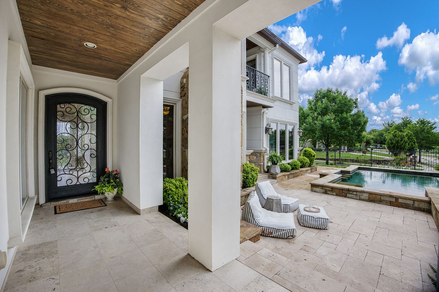 Front entrance porch of luxury modern home with iron door and stone pavers overlooking swimming pool and landscaping.