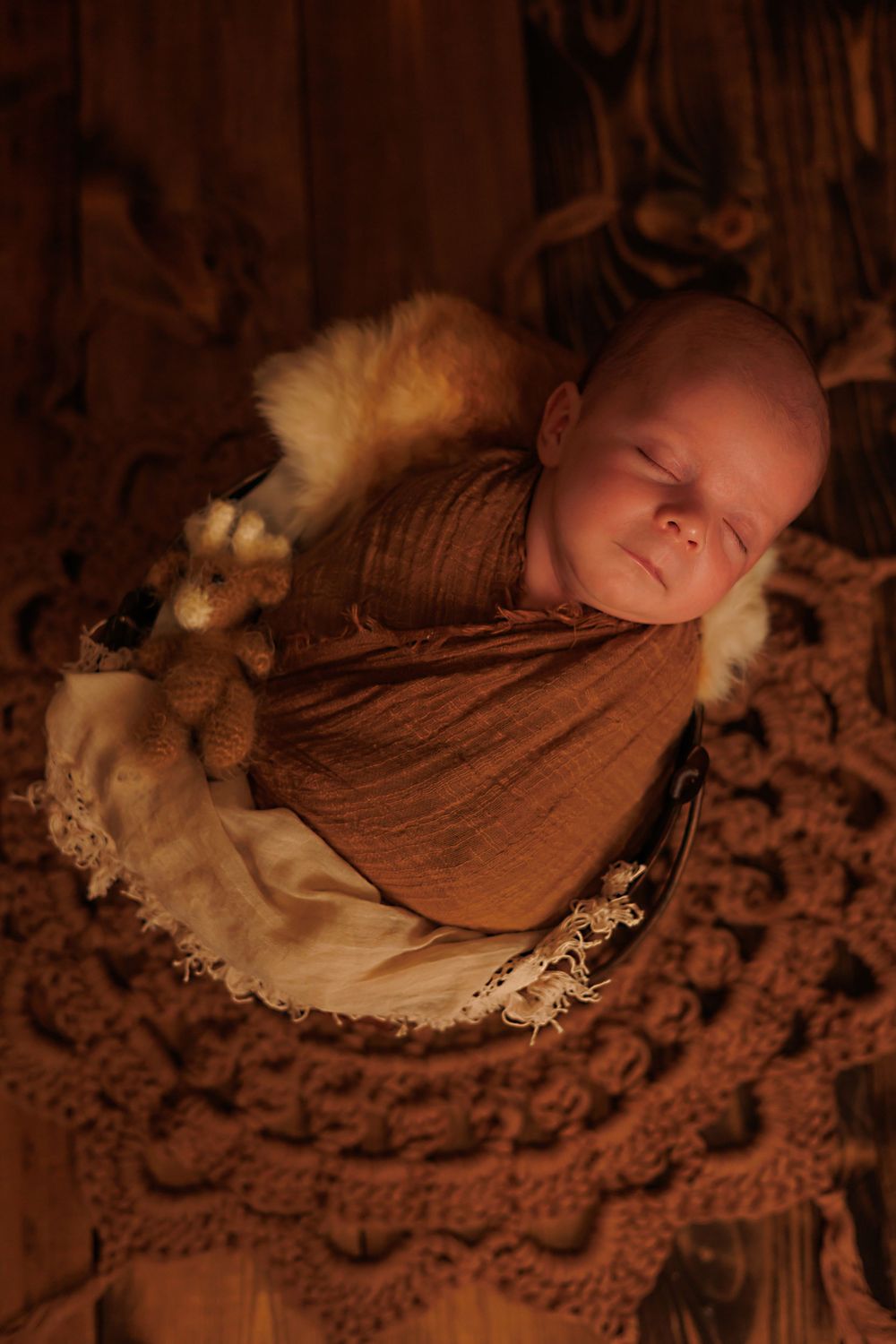 Newborn sleeping on textured brown lace blanket in moody lighting.