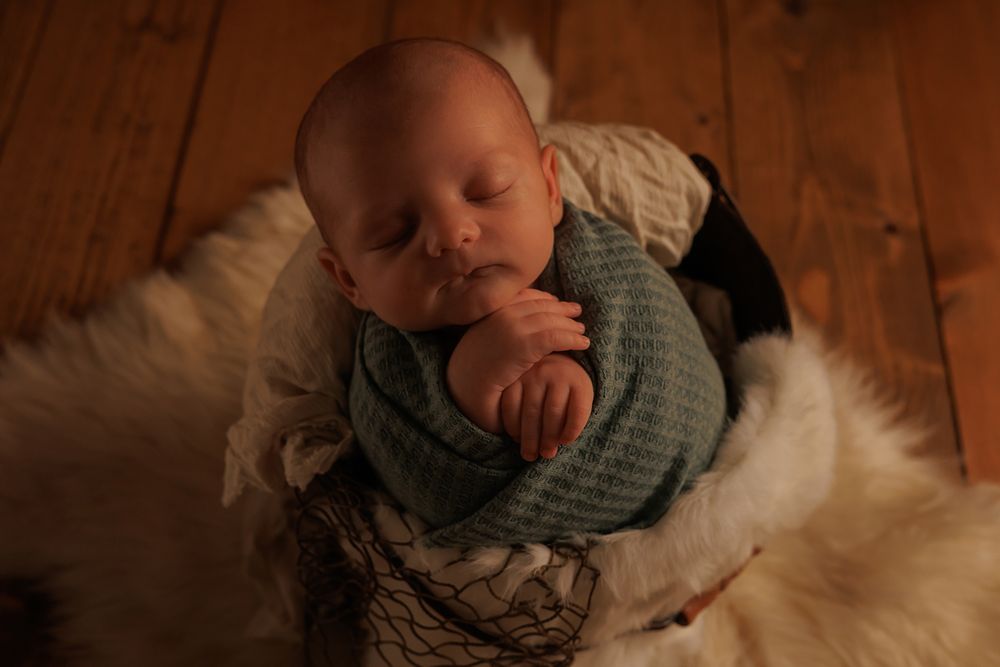 Sleeping baby lying on wooden floor with soft blanket.
