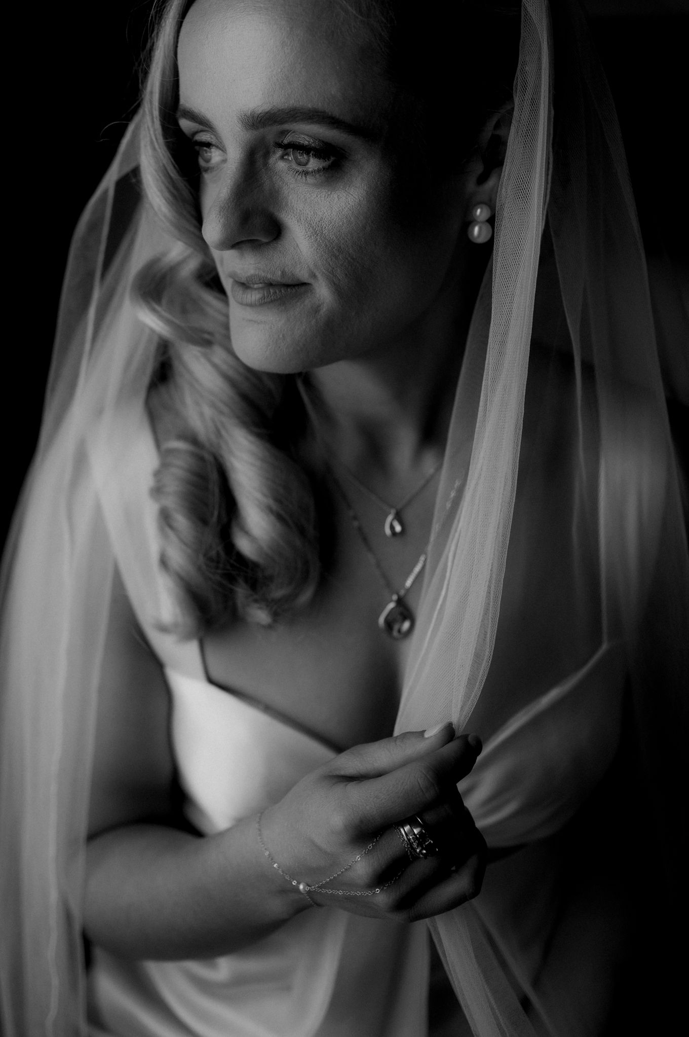 Black and white portrait of a bride in veil with delicate jewelry, wrapped in soft ethereal lighting.