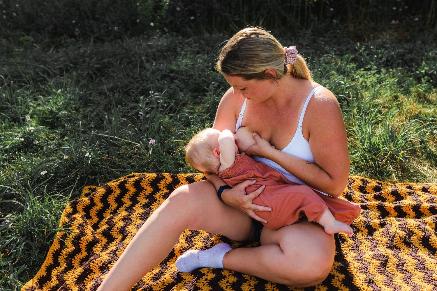 Mother nursing infant on an orange and black patterned blanket in summer.
