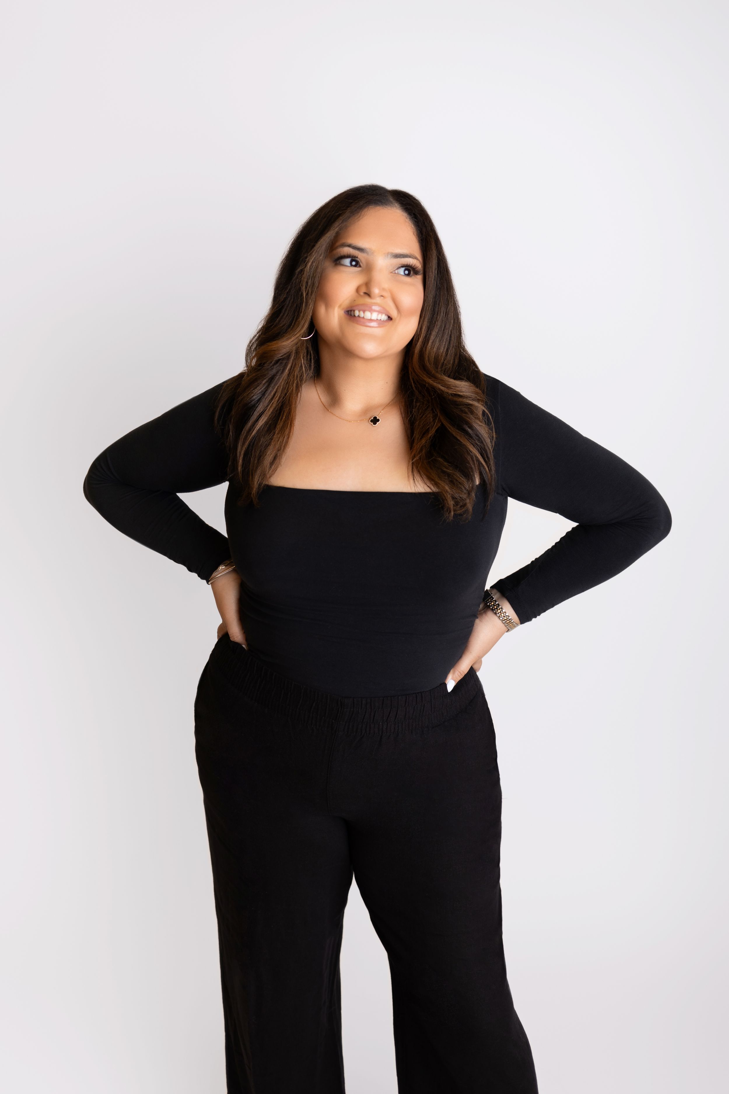 Professional shot of a woman in a sleek black outfit standing confidently against a white background. Branding Photoshoot Session in NJ