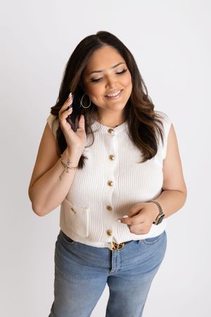 A person wearing a white ribbed sleeveless top and light blue jeans poses naturally in a photo studio setting.